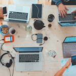 Schreibtisch aus Vogelperspektive mit mehreren Laptop, Stiften, Paier, etc.