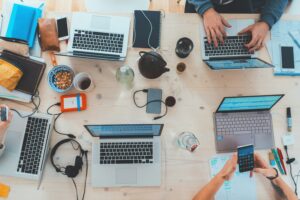 Schreibtisch aus Vogelperspektive mit mehreren Laptop, Stiften, Paier, etc.